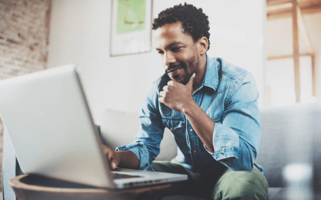 Photo of a man looking at his laptop while sitting on a couch