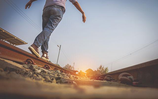 young man balancing on railroad track beam